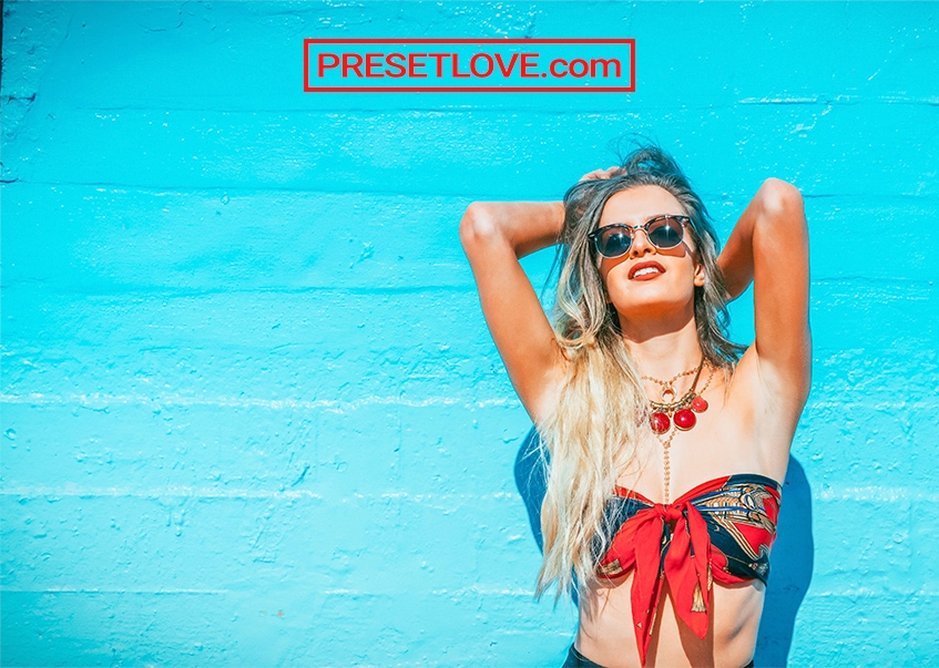 A high-contrast summer portrait of a woman in red bikini against a blue wall