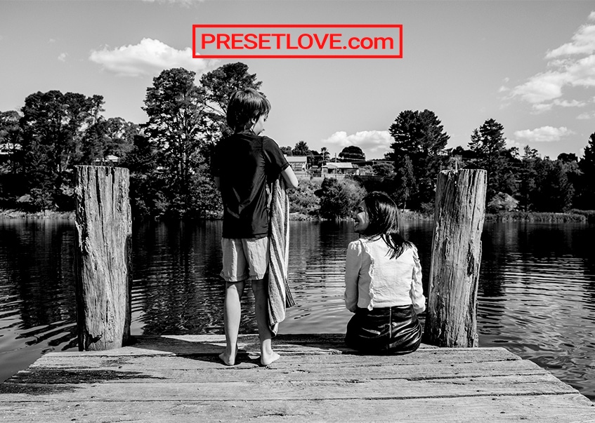 A black and white image of a boy and a woman talking by a river