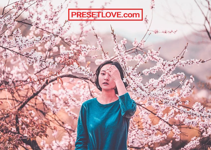 A woman's portrait with a cherry blossom tree in the background. with a free pink Lightroom preset applied.