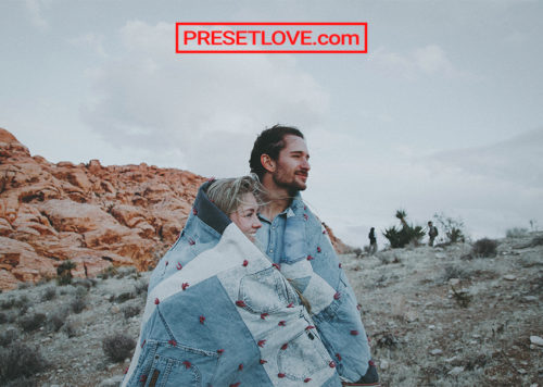 A retro outdoor portrait of a couple wrapped in denim quilt