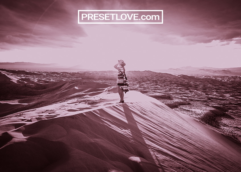A magenta- tinted photo of a woman in a desert