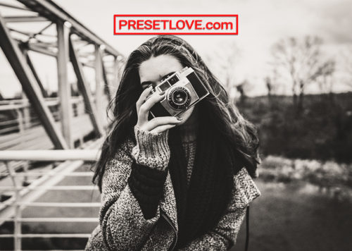 A warm black and white photo of a woman shooting with an analog camera