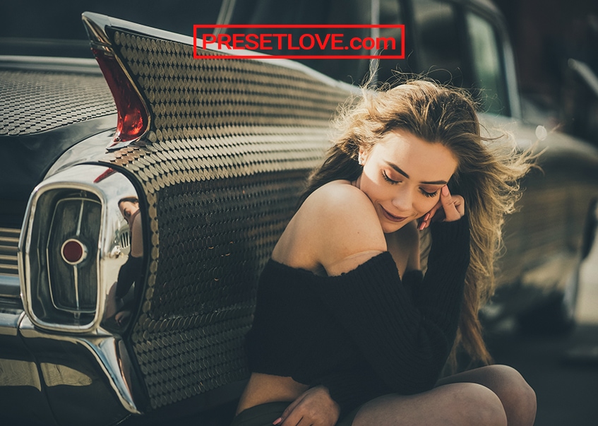 A cinematic photo of a woman sitting down and leaning beside a vintage car