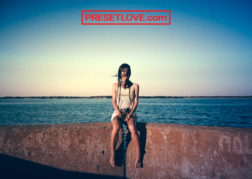 A retro outdoor photo of a woman with the ocean behind her