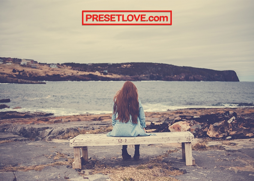 A yellowish photo of a woman sitting on a bench facing the sea