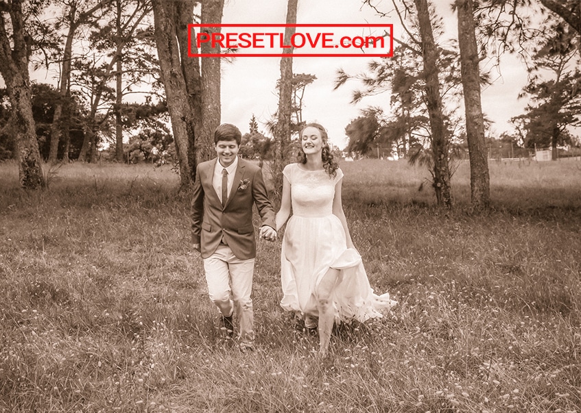 A sepia monochrome photo of a couple walking across a field